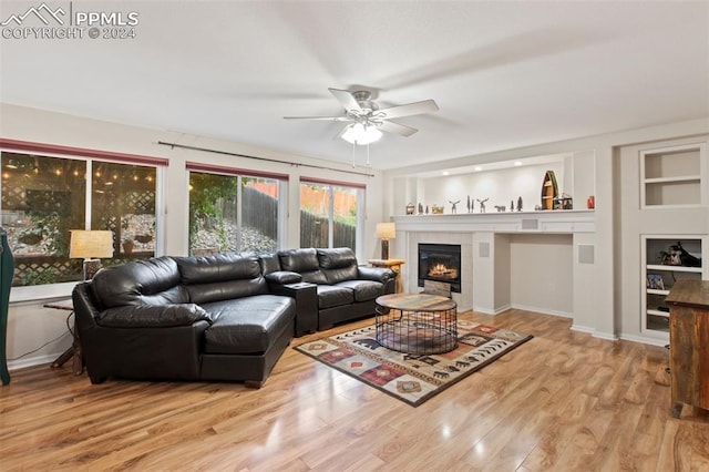 living room featuring ceiling fan, light hardwood / wood-style floors, a fireplace, and built in shelves