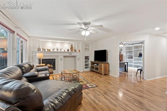 living room featuring hardwood / wood-style floors, ceiling fan, built in shelves, and a tiled fireplace