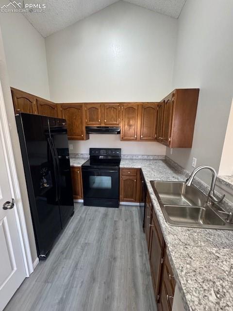 kitchen featuring high vaulted ceiling, black appliances, sink, light hardwood / wood-style flooring, and a textured ceiling