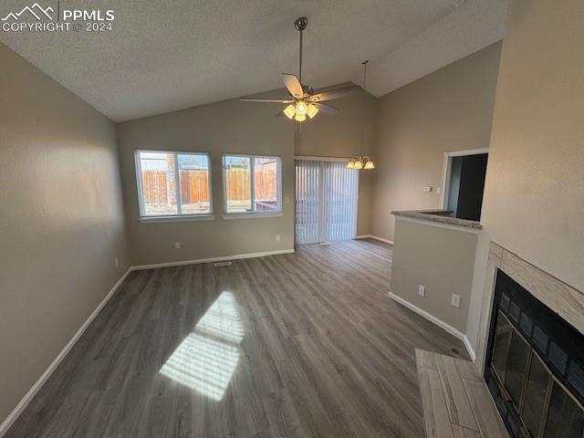 unfurnished living room with lofted ceiling, ceiling fan with notable chandelier, dark hardwood / wood-style floors, and a textured ceiling