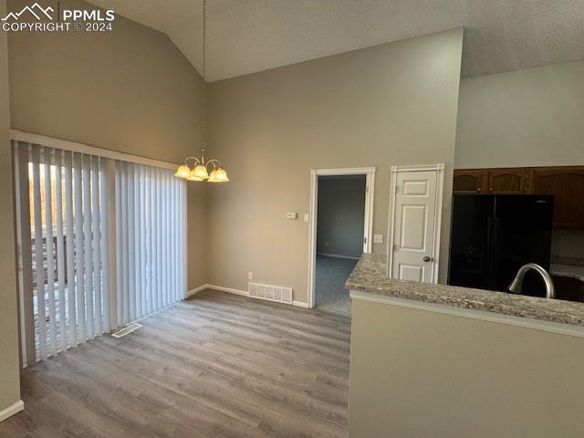 unfurnished living room featuring a notable chandelier, sink, light hardwood / wood-style flooring, and vaulted ceiling