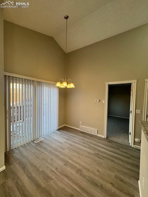 unfurnished dining area with hardwood / wood-style floors, an inviting chandelier, a textured ceiling, and vaulted ceiling