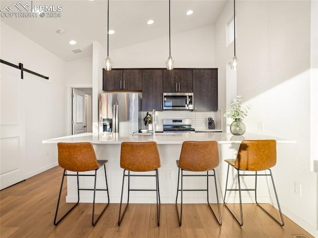 kitchen featuring dark brown cabinetry, a barn door, light hardwood / wood-style flooring, a breakfast bar, and appliances with stainless steel finishes