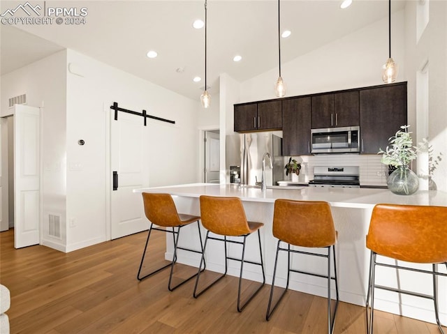 kitchen featuring a breakfast bar area, light hardwood / wood-style flooring, a barn door, dark brown cabinets, and stainless steel appliances