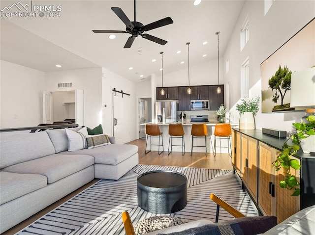 living room with a barn door, light hardwood / wood-style flooring, high vaulted ceiling, and ceiling fan