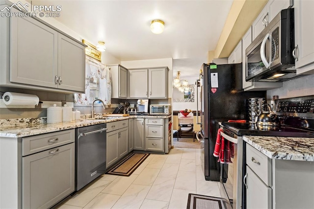 kitchen featuring light stone counters, stainless steel appliances, gray cabinets, and sink