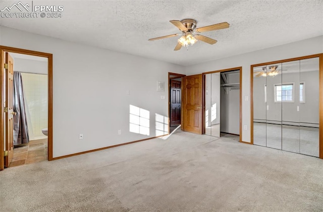 unfurnished bedroom featuring a textured ceiling, connected bathroom, two closets, and light colored carpet