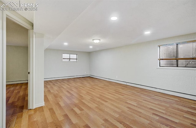 basement with baseboard heating and light hardwood / wood-style flooring