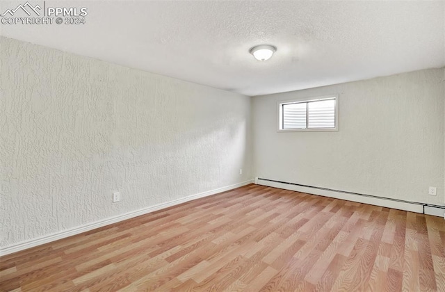 unfurnished room with baseboard heating, a textured ceiling, and light wood-type flooring