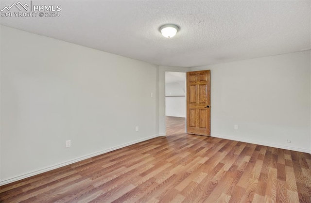 empty room with a textured ceiling and light hardwood / wood-style flooring