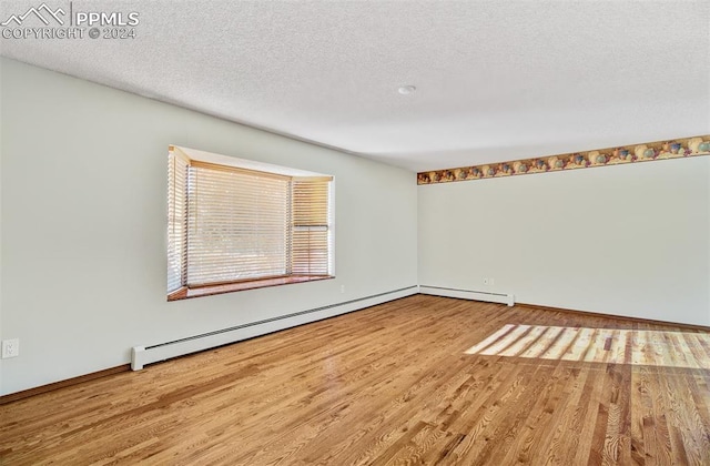 unfurnished room with hardwood / wood-style floors, a textured ceiling, and a baseboard heating unit