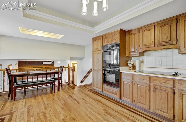 kitchen with black appliances, light hardwood / wood-style floors, backsplash, and a tray ceiling