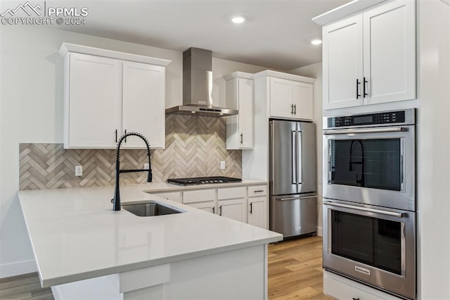 kitchen with wall chimney exhaust hood, white cabinetry, appliances with stainless steel finishes, and light hardwood / wood-style flooring