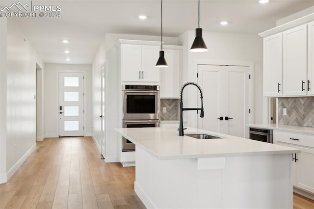 kitchen with a center island with sink, decorative backsplash, and double oven