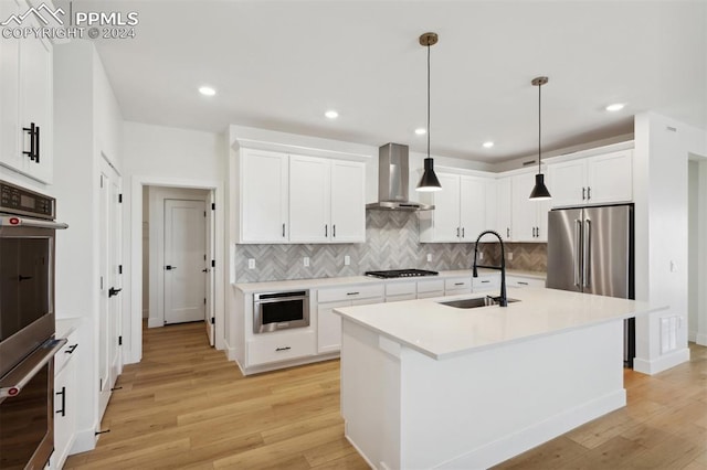 kitchen featuring pendant lighting, light wood-type flooring, wall chimney exhaust hood, and sink