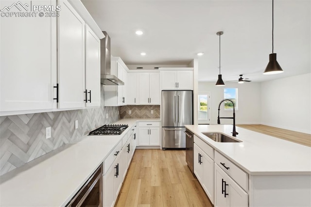 kitchen featuring white cabinetry, sink, wall chimney exhaust hood, stainless steel appliances, and pendant lighting