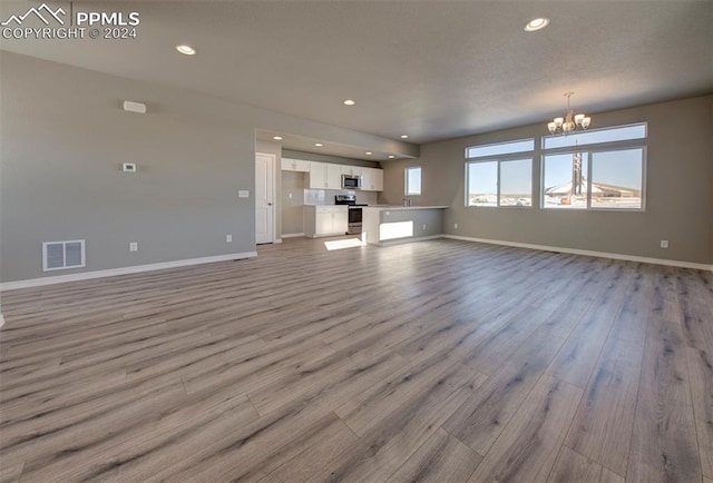 unfurnished living room with light hardwood / wood-style flooring and a chandelier