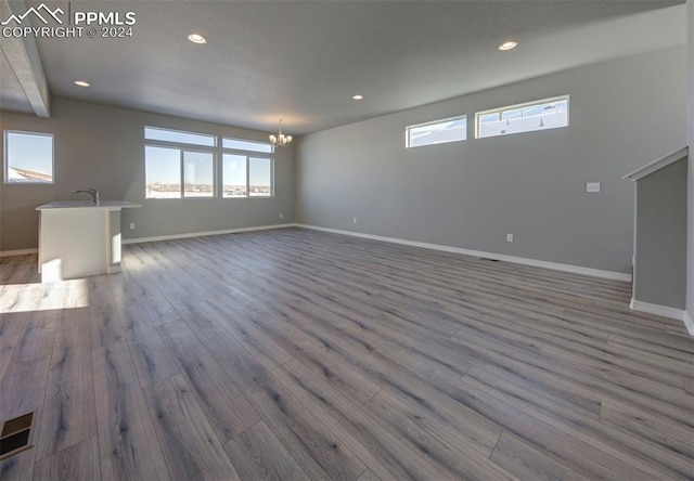 unfurnished living room featuring beamed ceiling, light wood-type flooring, an inviting chandelier, and sink