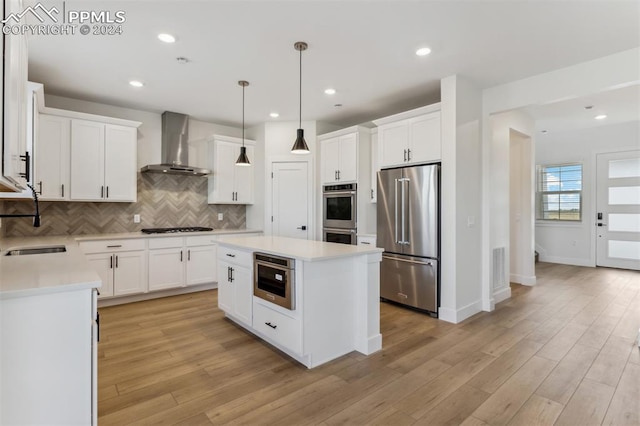 kitchen featuring white cabinetry, wall chimney exhaust hood, light wood-type flooring, and appliances with stainless steel finishes