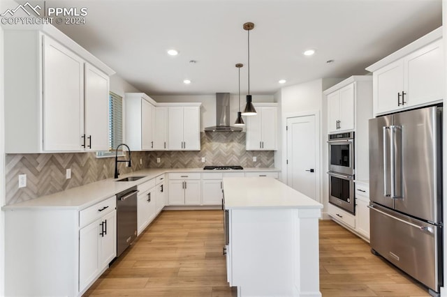 kitchen featuring pendant lighting, a center island, wall chimney range hood, sink, and stainless steel appliances