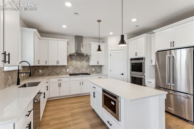 kitchen featuring a center island, wall chimney range hood, sink, white cabinetry, and stainless steel appliances