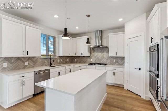 kitchen featuring sink, wall chimney exhaust hood, appliances with stainless steel finishes, a kitchen island, and white cabinetry