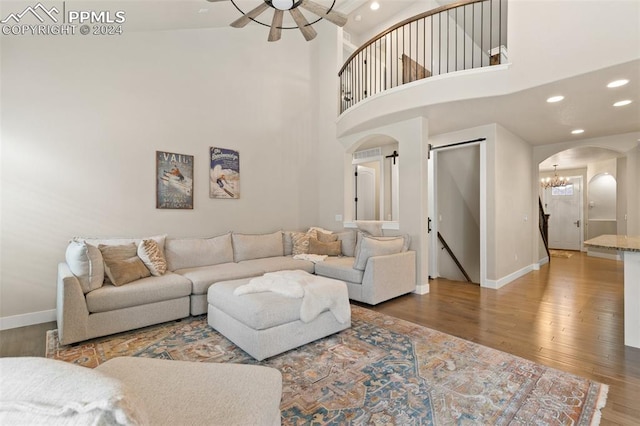 living room with hardwood / wood-style floors, a towering ceiling, and ceiling fan with notable chandelier