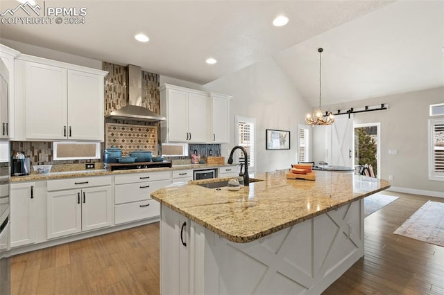 kitchen featuring white cabinetry, sink, wall chimney range hood, a barn door, and an island with sink