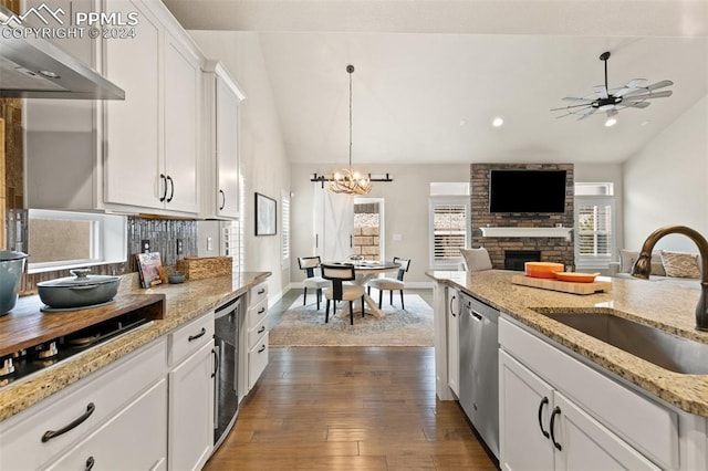 kitchen with light stone counters, sink, exhaust hood, white cabinets, and a stone fireplace