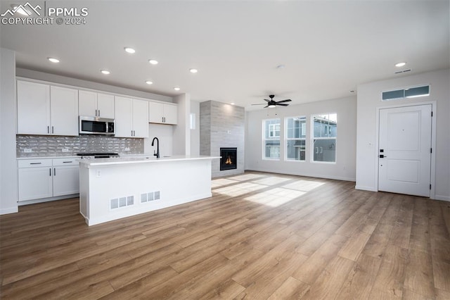 kitchen featuring ceiling fan, backsplash, a fireplace, white cabinets, and a center island with sink