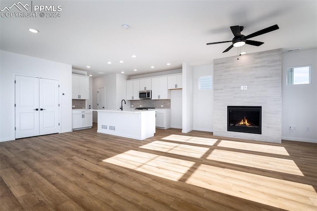 unfurnished living room featuring a tiled fireplace, ceiling fan, sink, and light hardwood / wood-style floors