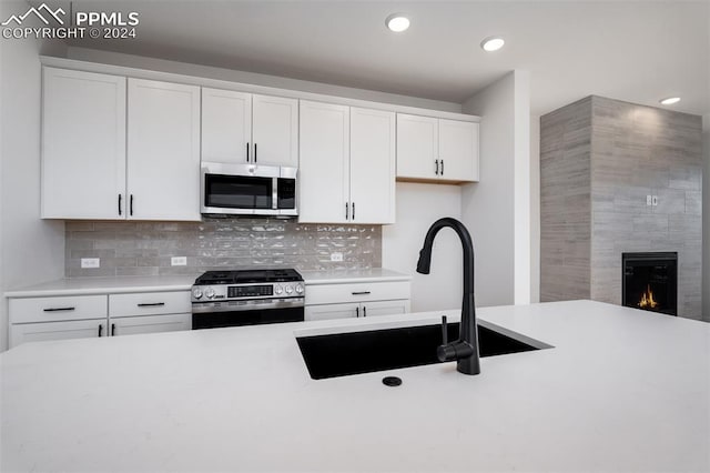 kitchen featuring a tile fireplace, white cabinetry, sink, and appliances with stainless steel finishes