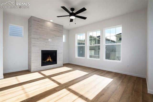 unfurnished living room featuring hardwood / wood-style floors, ceiling fan, and a tiled fireplace