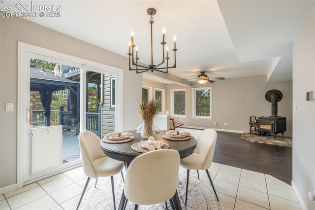 dining area with ceiling fan with notable chandelier, light tile patterned flooring, and a wood stove