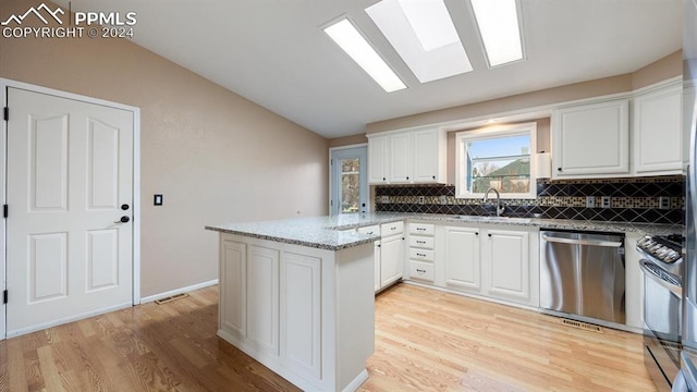 kitchen with kitchen peninsula, appliances with stainless steel finishes, white cabinetry, and light stone countertops