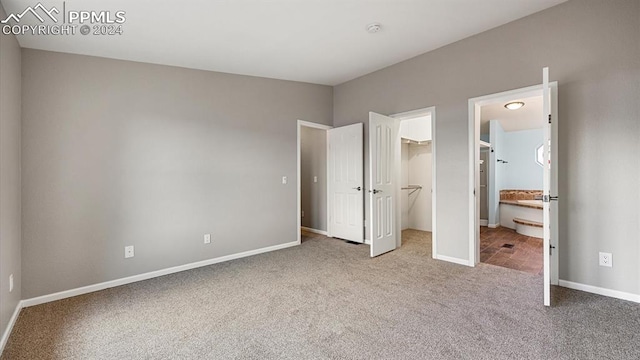 unfurnished bedroom featuring ensuite bathroom, a spacious closet, a closet, and light colored carpet