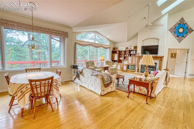 living room featuring light wood-type flooring, a skylight, high vaulted ceiling, and ceiling fan