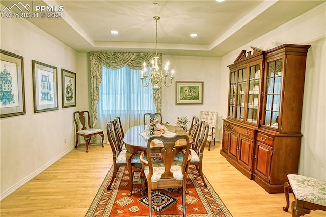 dining area with a notable chandelier, a raised ceiling, and light hardwood / wood-style flooring