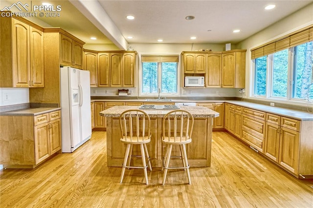 kitchen featuring sink, a center island, light hardwood / wood-style flooring, white appliances, and a breakfast bar area