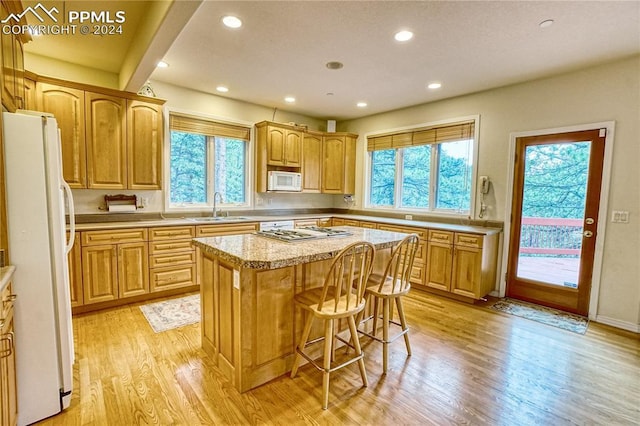 kitchen with sink, a kitchen breakfast bar, white appliances, a kitchen island, and light wood-type flooring