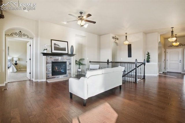 living room with a stone fireplace, ceiling fan, and dark wood-type flooring