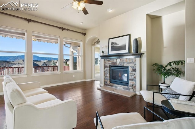 living room with a stone fireplace, a mountain view, ceiling fan, and dark wood-type flooring