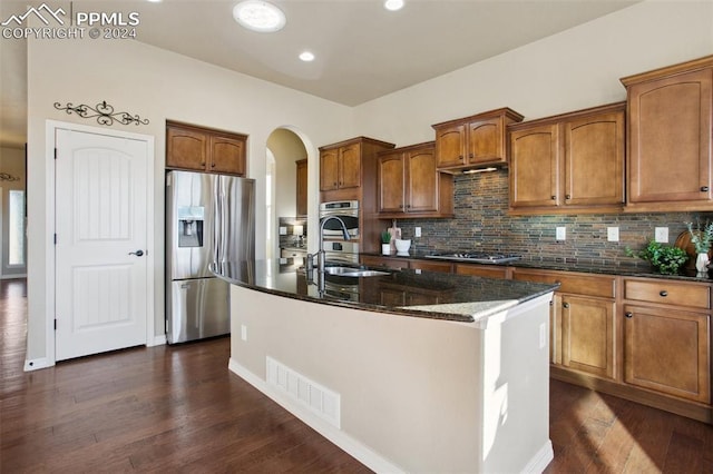 kitchen featuring dark stone countertops, a kitchen island with sink, dark hardwood / wood-style floors, and appliances with stainless steel finishes