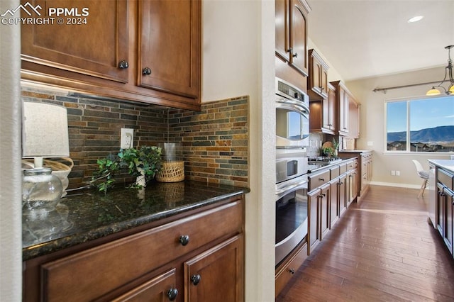 kitchen with a mountain view, backsplash, dark stone counters, hanging light fixtures, and dark hardwood / wood-style flooring