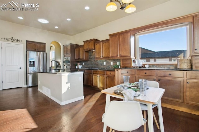 kitchen featuring decorative backsplash, dark hardwood / wood-style flooring, an island with sink, and appliances with stainless steel finishes