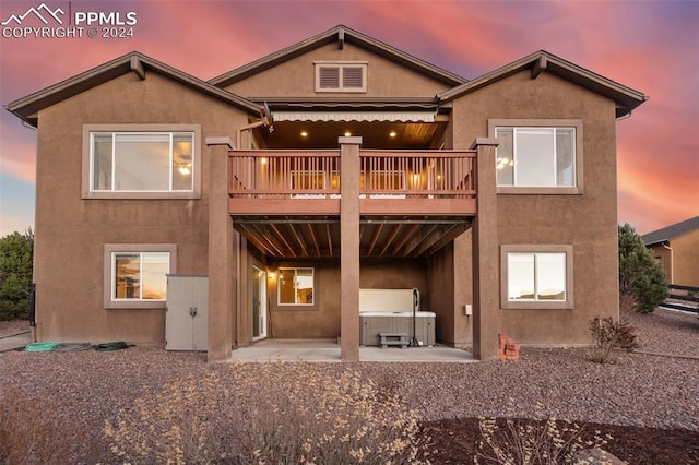 back house at dusk with a patio, a hot tub, and a deck