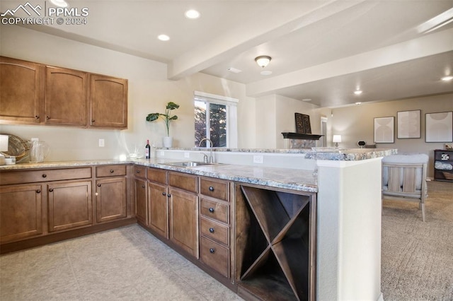 kitchen featuring light carpet, sink, beamed ceiling, light stone counters, and kitchen peninsula