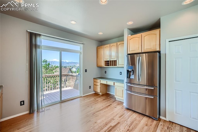 kitchen featuring light wood-type flooring, stainless steel refrigerator with ice dispenser, built in desk, and light brown cabinets