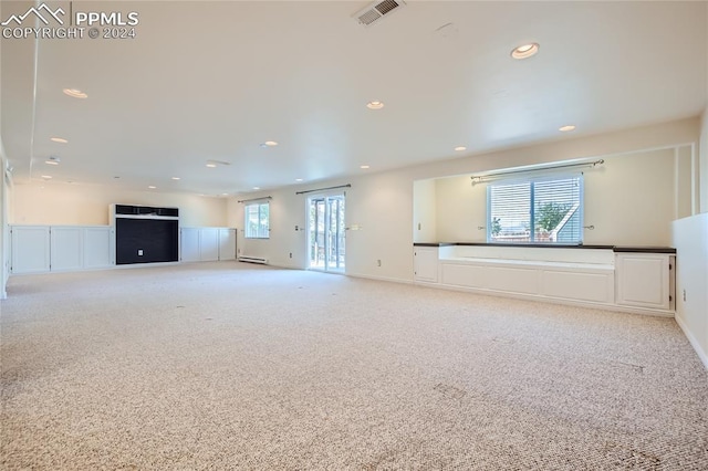 unfurnished living room featuring light carpet, a healthy amount of sunlight, and a baseboard heating unit