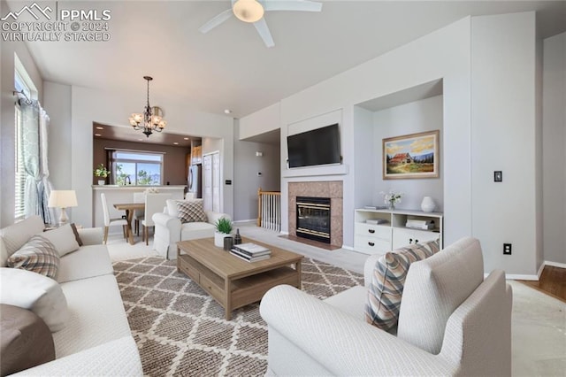 living room featuring a tile fireplace and ceiling fan with notable chandelier